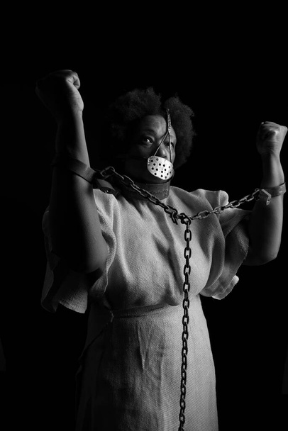 Портрет черной женщины в железной маске на лице, чтобы олицетворять боль рабыни Анастасии. Изолированный на черном фоне - Фото, изображение