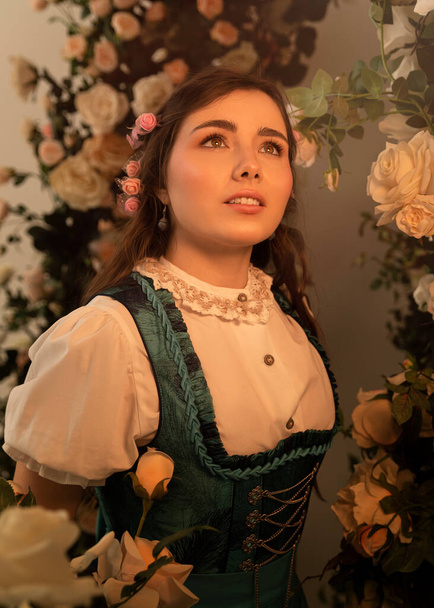 A young peasant woman standing in a garden with flowers dressed in a 19th century bavarian dress. - Фото, изображение
