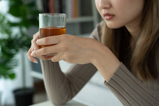 Депрессивная молодая азиатская женщина, которая чувствует себя плохо, выпивая виски в одиночестве дома, подчеркнула, что разочарованная одинокая пьющая алкоголь страдает от проблем с алкоголем, алкоголизмом, жизнью и семейными проблемами - Фото, изображение