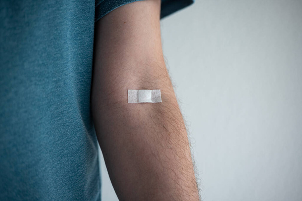 Small plaster or bandaid on the arm of an unrecognizable Caucasian male. Plastered on the elbow pit to stop bleeding after blood collection. - Photo, image