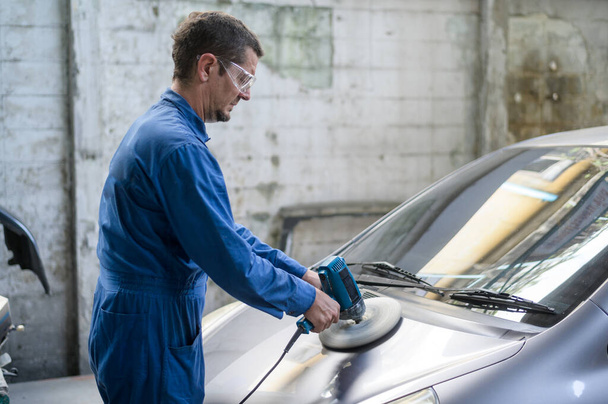 Caucasian man is using car polishing machine in repair mechanic painting shop  - Fotó, kép