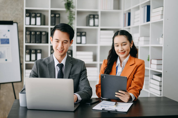 Asiatische Geschäftsleute präsentieren und erklären Laptop und Tablet. Teamarbeit, Finanzmarketing-Team, während man im modernen Bürozimmer sitzt. - Foto, Bild