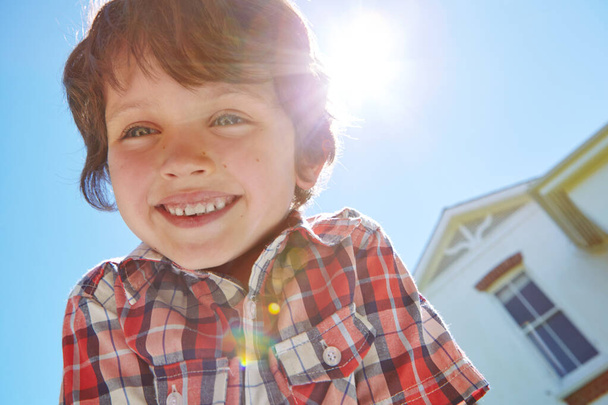 Blue skies and bright smiles. Low angle portrait of a young boy outdoors with his home in the background - Foto, immagini