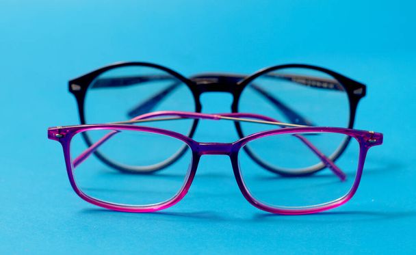 Nahaufnahme lebhafter rosa und schwarzer Brillengestelle aus Kunststoff auf blauem Hintergrund - Foto, Bild