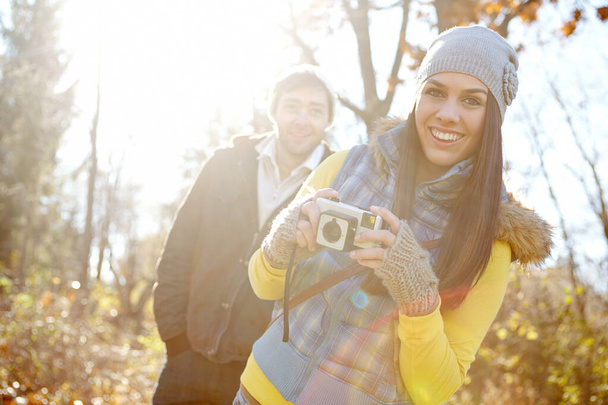 We should do this more often. A young woman holding a camera with her boyfriend standing in the background - Foto, imagen
