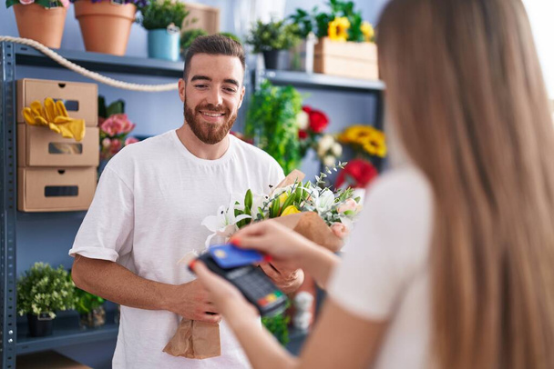 Man and woman customer buying bouquet of flower by credit card at flower shop - Foto, immagini