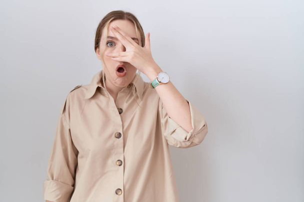 Mujer caucásica joven con camisa casual que mira con la mano a través de los dedos con expresión avergonzada.  - Foto, Imagen