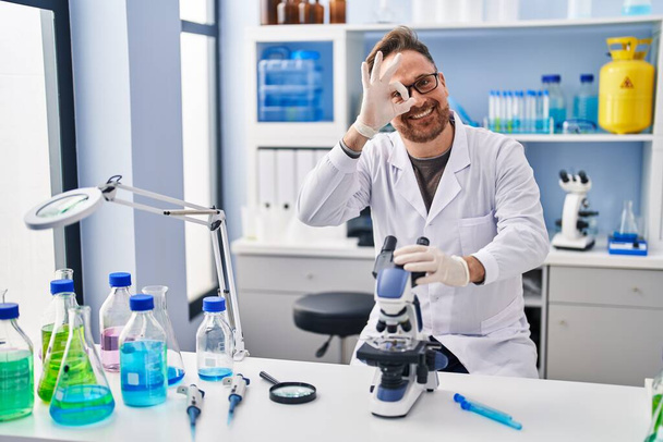 Středověký běloch pracující v laboratoři vědec s úsměvem šťastný dělá ok znamení s rukou na oku dívá skrz prsty  - Fotografie, Obrázek
