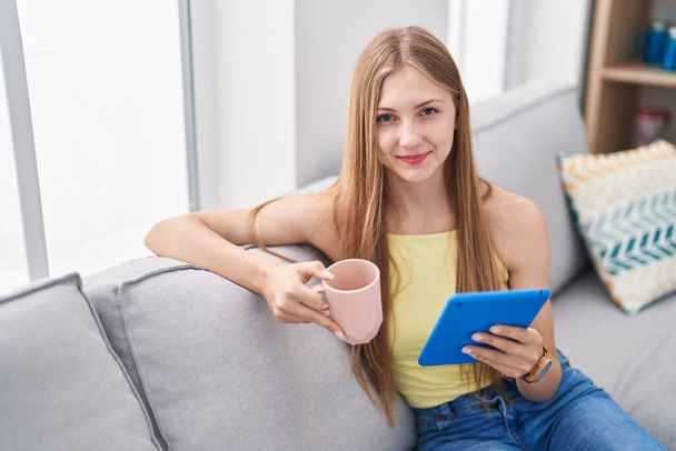 Young caucasian woman drinking coffee using touchpad at home - Foto, Bild