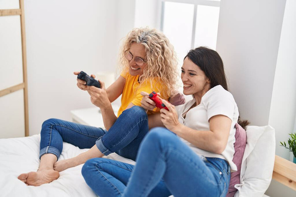 二人の女性母と娘再生ビデオゲーム座っています上のベッドルーム - 写真・画像