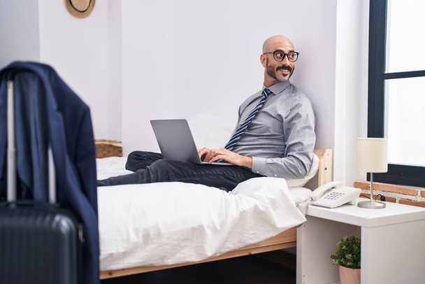 Jonge Spaanse zakenman met laptop op bed in hotelkamer - Foto, afbeelding