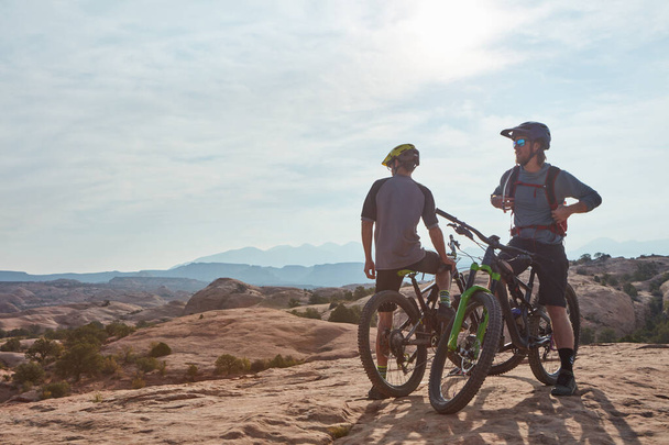 Milhas e milhas de sorrisos. Tiro de comprimento total de dois homens atléticos fazendo uma pausa para admirar a vista, enquanto a montanha de bicicleta através do deserto - Foto, Imagem