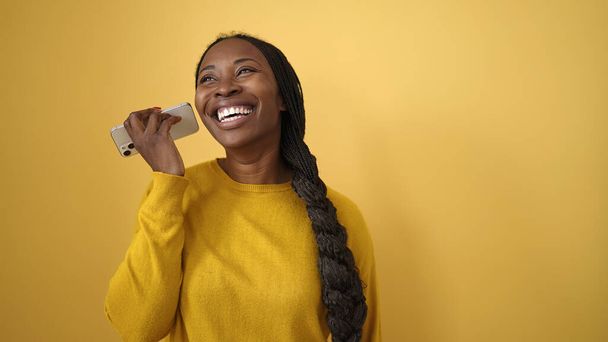 Femme africaine écoutant un message vocal au téléphone sur fond jaune isolé - Photo, image