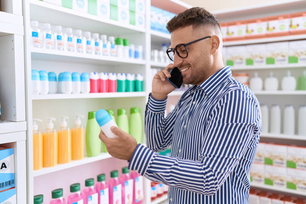 Jovem hispânico homem cliente falando no smartphone segurando desodorizante na farmácia - Foto, Imagem