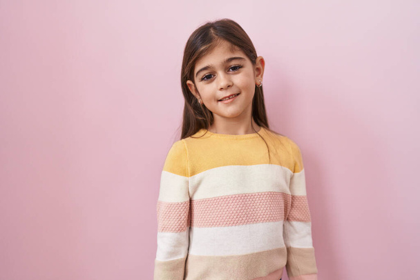 Niña hispana usando suéter sobre fondo rosa con una sonrisa alegre y fresca en la cara. persona afortunada.  - Foto, Imagen