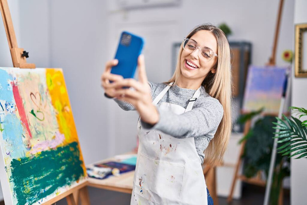 Young woman artist smiling confident making selfie by the smartphone at art studio - Photo, image