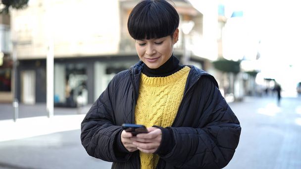 Fiatal kínai nő mosolygós magabiztos segítségével smartphone az utcán - Fotó, kép