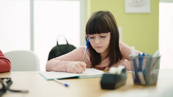 Adorable estudiante hispana escribiendo en un cuaderno en el aula - Foto, imagen
