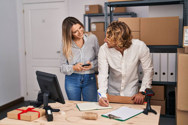 Чоловік і жінка електронної комерції бізнес-працівники пишуть на книзі, використовуючи смартфон в офісі
 - Фото, зображення