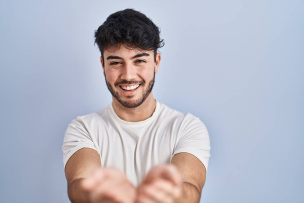Hispanic man with beard standing over white background smiling with hands palms together receiving or giving gesture. hold and protection  - Foto, Bild