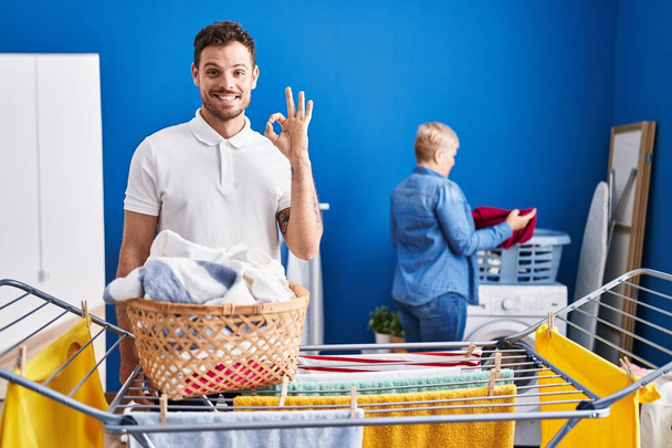 Hispanic mother and son hanging clothes at clothesline doing ok sign with fingers, smiling friendly gesturing excellent symbol  - Фото, зображення
