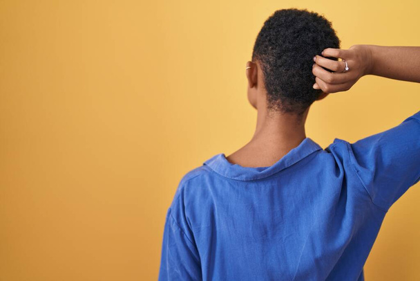 African american woman standing over yellow background backwards thinking about doubt with hand on head  - Foto, Bild