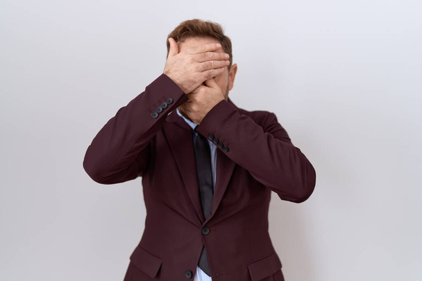 Middle age business man with beard wearing suit and tie covering eyes and mouth with hands, surprised and shocked. hiding emotion  - Foto, Imagem