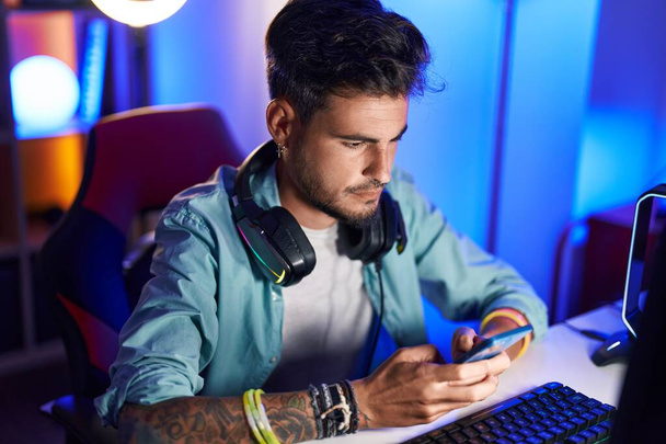 Junger hispanischer Mann streamt mit Computer und Smartphone in Spielhalle - Foto, Bild
