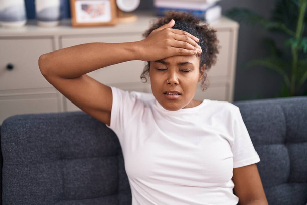 Afroamerikanerin leidet unter Kopfschmerzen, wenn sie zu Hause auf dem Sofa sitzt - Foto, Bild