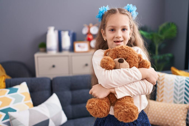 Αξιολάτρευτο καυκάσιο κορίτσι χαμογελά αυτοπεποίθηση αγκαλιάζει αρκουδάκι στο σπίτι - Φωτογραφία, εικόνα