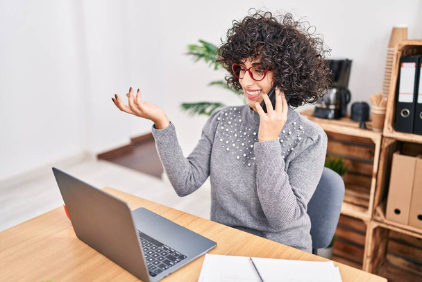 Joven mujer de Oriente Medio trabajador de negocios utilizando portátil hablando en el teléfono inteligente en la oficina - Foto, imagen