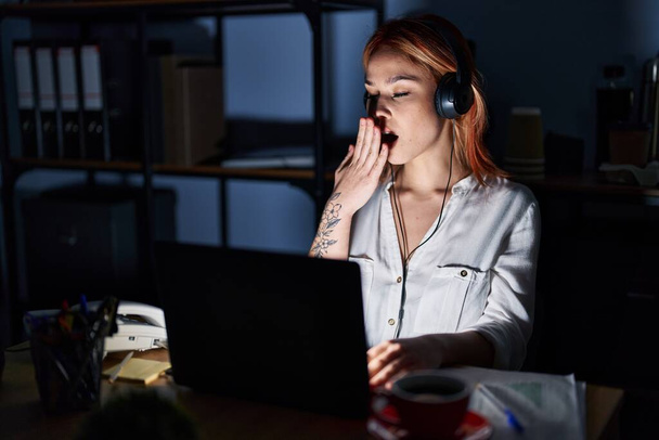夜のオフィスで働いていた若い白人女性は、手で口を覆い疲れたあくびを退屈させた。落ち着きもなく眠気もなく.  - 写真・画像