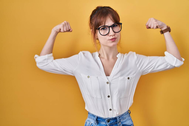 Young beautiful woman wearing casual shirt over yellow background showing arms muscles smiling proud. fitness concept.  - Foto, Imagem