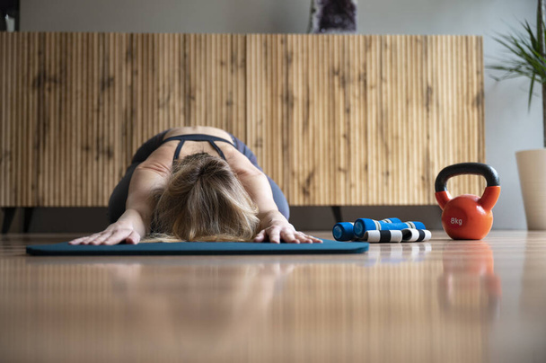 Lage hoek vooraanzicht van een vrouw stretching in kind poseren na een thuistraining of pilates routine. Op een trainingsmat in de huiskamer. - Foto, afbeelding