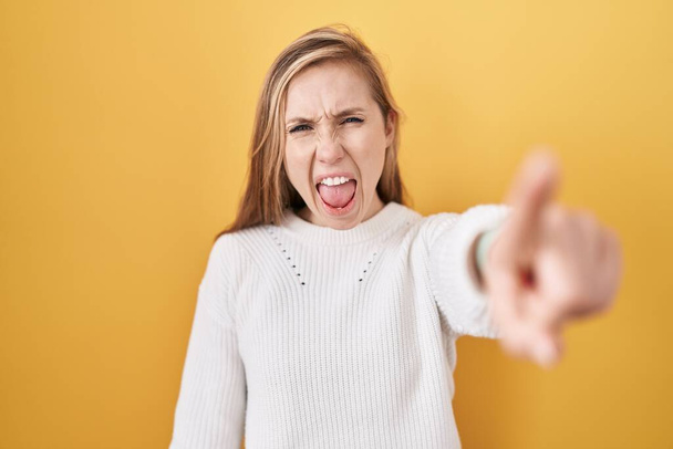 Young caucasian woman wearing white sweater over yellow background pointing displeased and frustrated to the camera, angry and furious with you  - Photo, image