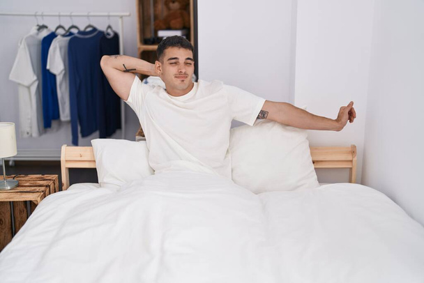 Молодой латиноамериканец просыпается с протянутыми руками в спальне - Фото, изображение