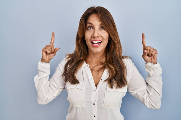 Hispanic woman standing over isolated background smiling amazed and surprised and pointing up with fingers and raised arms.  - Photo, Image