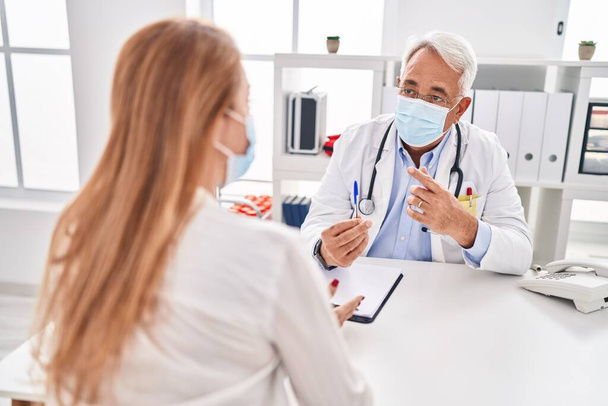 Middle age man and woman doctor and patient wearing medical mask having consultation at clinic - Photo, Image