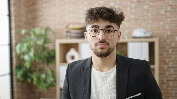 Young arab man business worker standing with relaxed expression at office - Фото, изображение