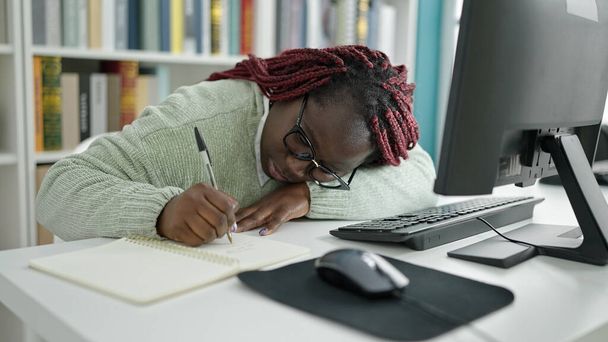 Mujer africana con pelo trenzado estudiante escribir notas cansado en la biblioteca universitaria - Foto, imagen