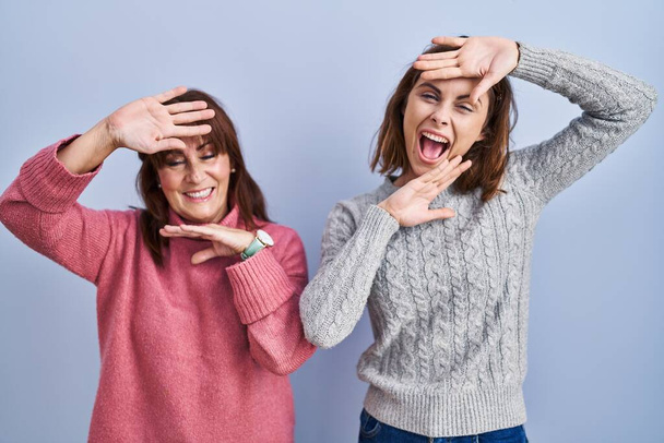 Mother and daughter standing over blue background smiling cheerful playing peek a boo with hands showing face. surprised and exited  - Foto, imagen