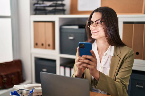 Νεαρή όμορφη Ισπανίδα επιχειρηματίας χρησιμοποιώντας smartphone που εργάζεται στο γραφείο - Φωτογραφία, εικόνα