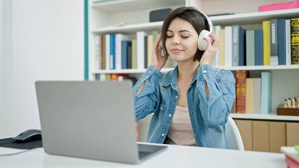 Young caucasian woman student using computer listening to music at university classroom - Foto, Imagen
