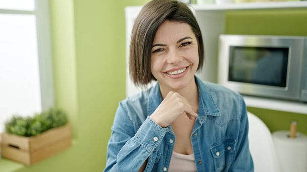 Young caucasian woman smiling confident sitting on table at home - 写真・画像