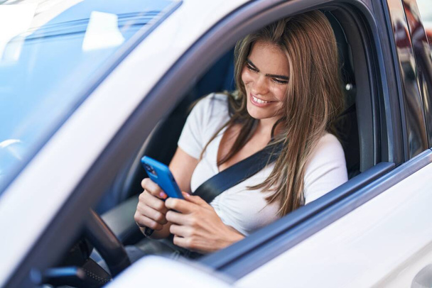 路上で車に座っているスマートフォンを使っている若い女性 - 写真・画像
