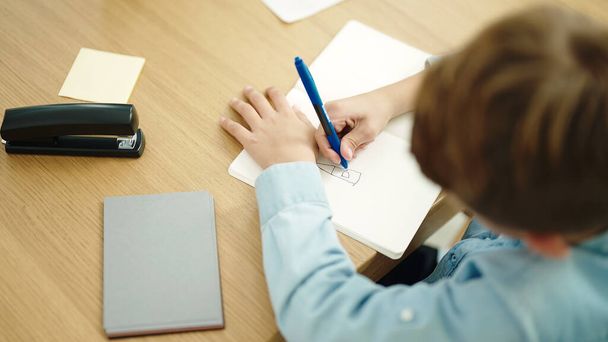 Imádnivaló kaukázusi fiú diák rajz notebook ül az asztalon az osztályteremben - Fotó, kép