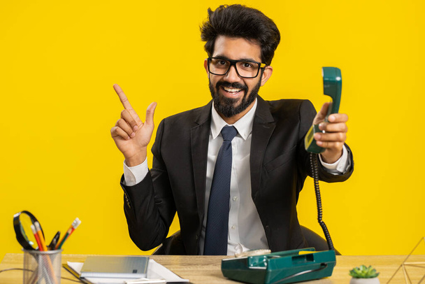 Rappelle-moi. Homme d'affaires indien parlant sur téléphone vintage rétro câblé des années 80 au bureau de travail. Hindou en costume officiel. Télécommande distante en ligne de travail sur ordinateur portable sur fond jaune - Photo, image