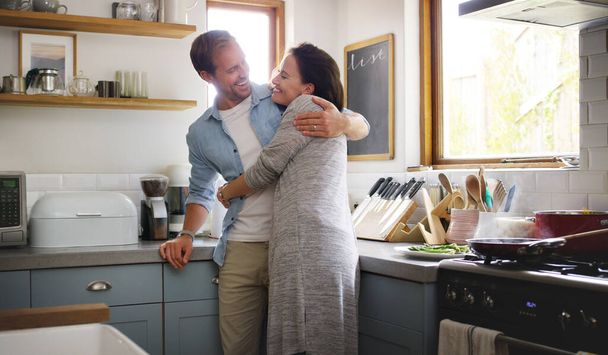 Still fond of those arms. an affectionate young couple embracing each other while standing in their kitchen at home - 写真・画像
