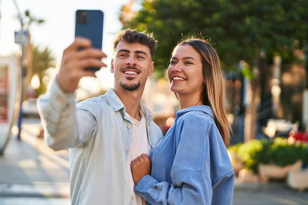 Fiatal férfi és nő pár mosolyog magabiztos, hogy szelfi az okostelefon az utcán - Fotó, kép