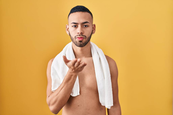 Jeune homme hispanique debout torse nu avec serviette regardant la caméra souffler un baiser avec la main sur l'air étant belle et sexy. expression d'amour.  - Photo, image